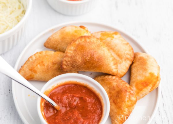 Homemade Air Fryer Pizza Rolls on a white plate with pizza sauce for dipping.