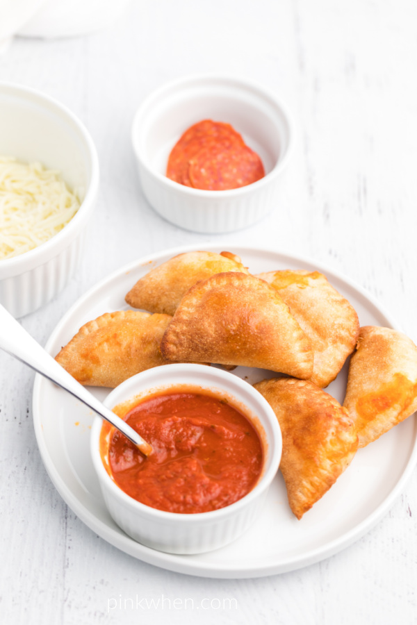 Pizza rolls on a white plate with extra pizza sauce for dipping the rolls. 