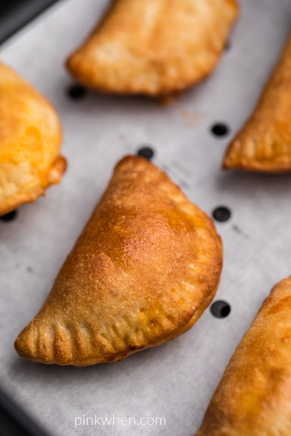 Close up image of homemade pizza rolls on parchment paper in the air fryer basket. 