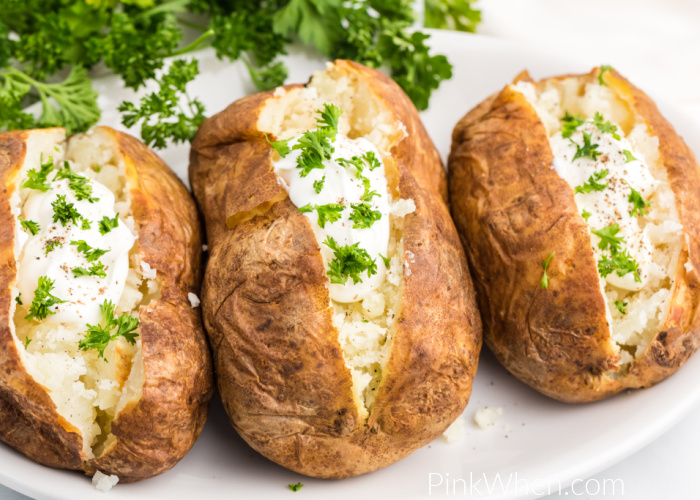 Air Fried baked potatoes on a white plate with sour cream and fresh parsley toppings. 