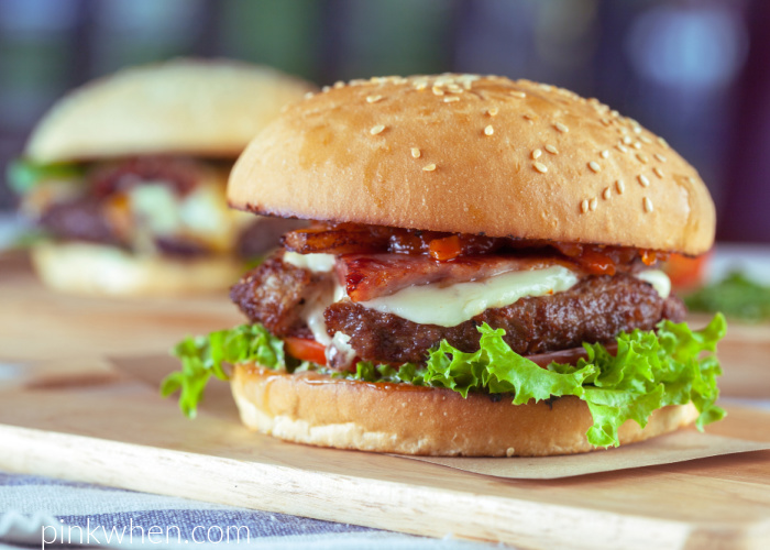 Air Fryer burger ready to eat and dressed on a bun with bacon, cheese, tomato, and lettuce. 