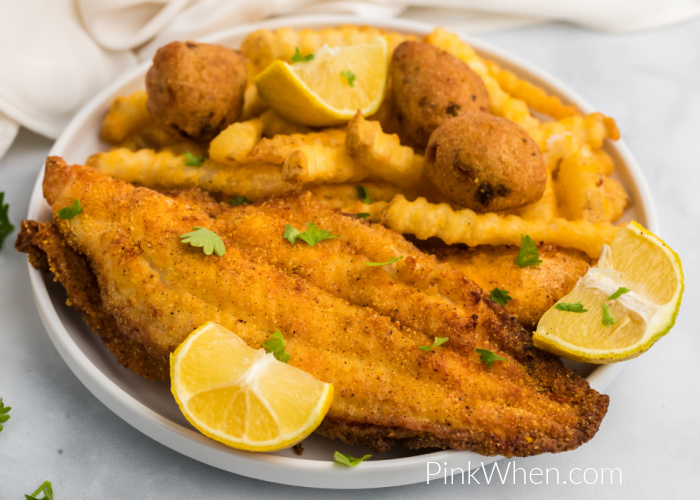 Air Fryer Catfish on a plate with french fries, hush puppies, and lemon wedges. 