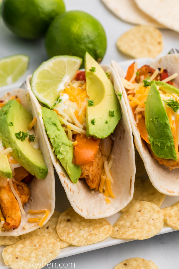 Close up photo of chicken fajitas on a plate with avocado, cheese, sour cream, and lime. 