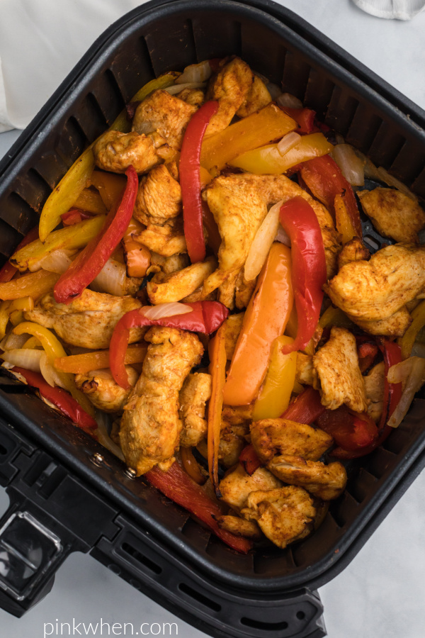 Fully cooked chicken fajitas and vegetables in the air fryer basket. 