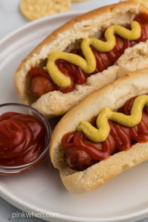 Close up photo of Air Fryer Hot Dogs with mustard and ketchup on a white plate ready to eat. 