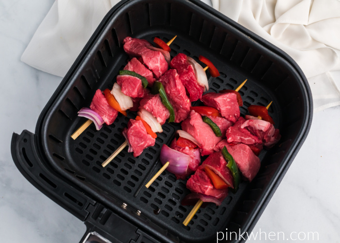Steak Kabobs with vegetables on wooden skewers in the bottom of an Air Fryer basket. 