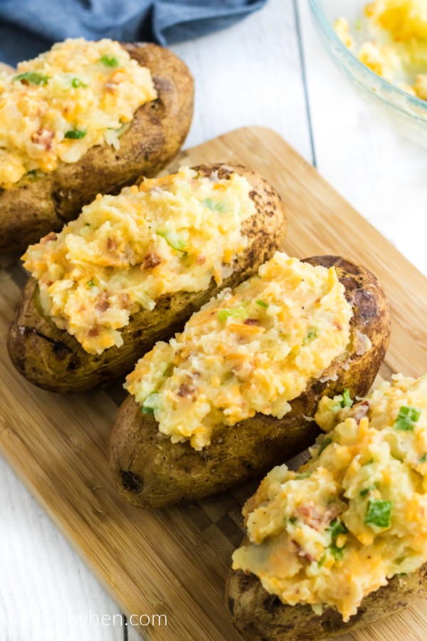 Twice Baked Potatoes stuffed and ready to eat while resting on a cutting board. 