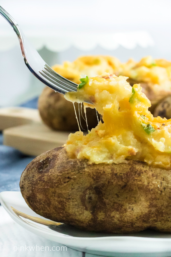 A bite on a fork from a twice baked potato thats resting on a white plate. 