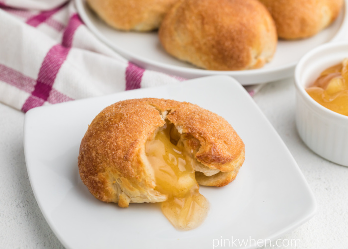 Apple Pie Bombs made in the air fryer in the background, in the foreground and apple pie bombs on a white plate with a bite missing. 