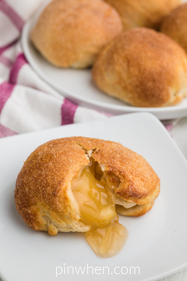 Apple Pie Bomb on a white plate with apple and glaze oozing out of the apple bomb. 
