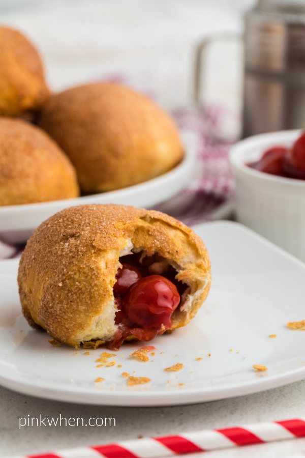 Air Fryer Cherry Pie Bomb on a white plate missing a bite with more cherry pie bombs in the background. 