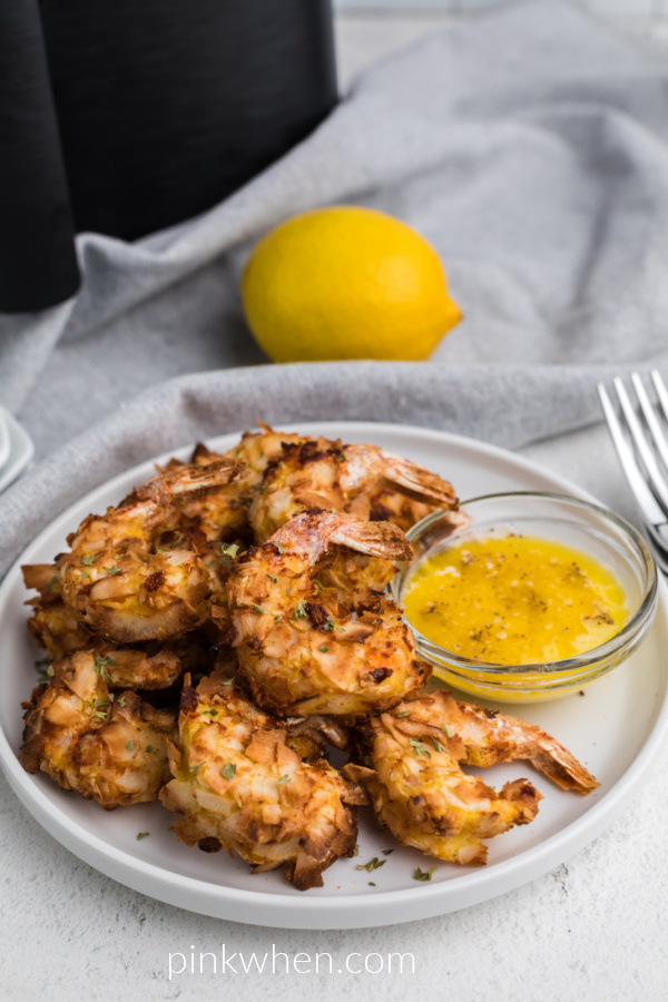 Coconut shrimp made in the air fryer and served on a white plate with a butter dipping sauce. 