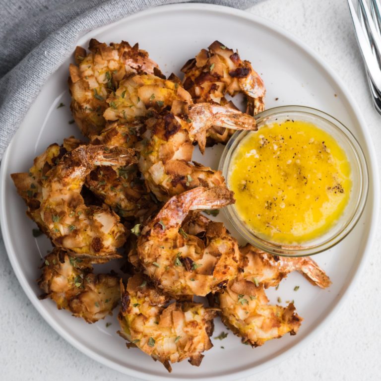 overhead photo of a plate of keto coconut shrimp on a white plate with a side or garlic butter sauce.