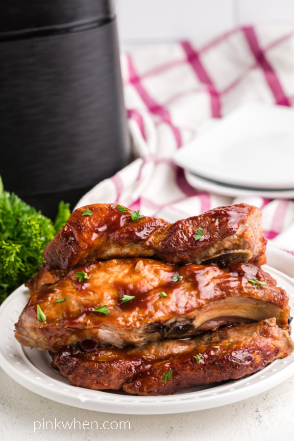 Country style ribs on a white plate with an air fryer in the background. 