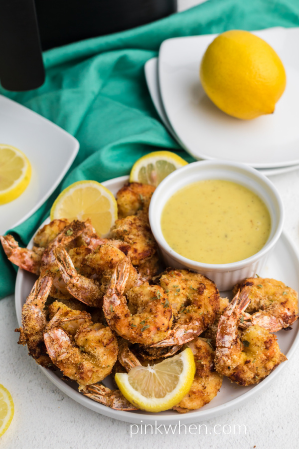 Fried shrimp made from the air fryer, served on a white plate with lemon slices and dipping sauce. 