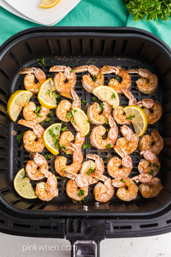 Lemon Pepper Shrimp and lemon wedges in the air fryer basket. 