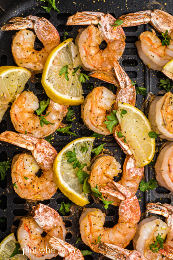 Air Fryer lemon pepper shrimp in the air fryer basket with lemon wedges and fresh parsley on top.