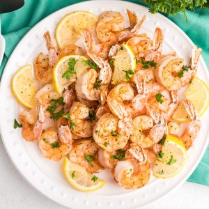 Overhead shot of air fryer lemon pepper shrimp on a white plate with lemon wedges and fresh parsley.