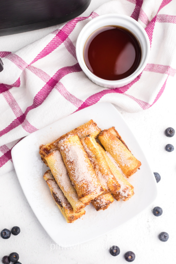 overhead shot of nutella french toast roll ups made in the air fryer - cooked and on a white plate with syrup for dipping on the side. 
