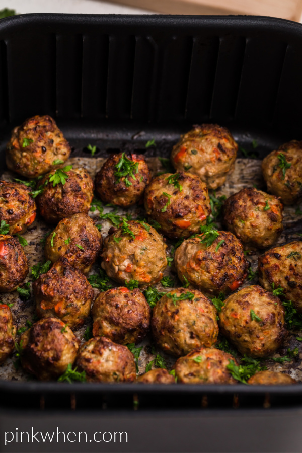 Turkey meatballs in the basket of the air fryer garnished with fresh parsley. 