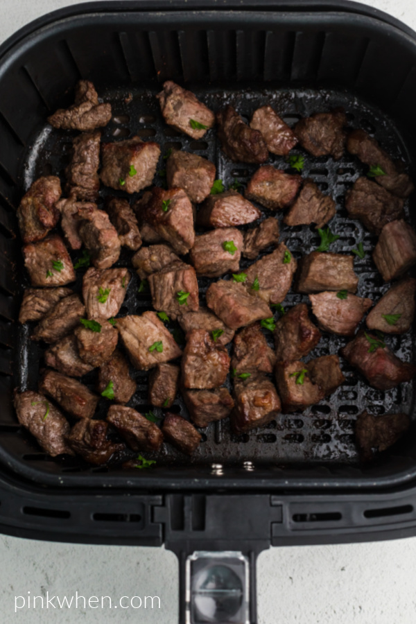 Cooked steak bites in the basket of the air fryer - topped with fresh chopped parsley. 