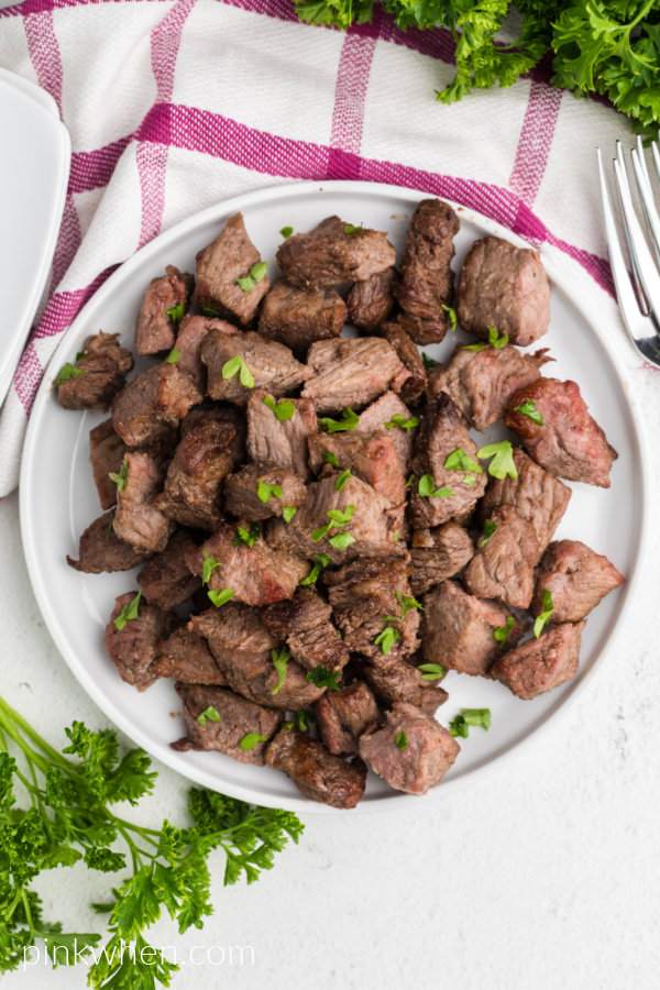 Overhead shot of air fryer garlic butter steak bites on a white plate ready to serve. 