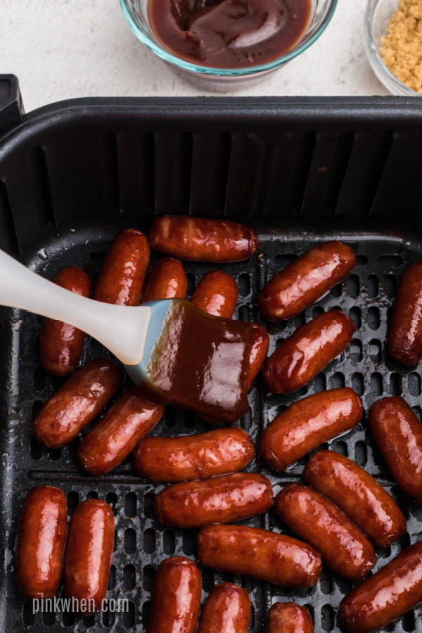 Brushing BBQ sauce on the little smokies in the air fryer basket. 