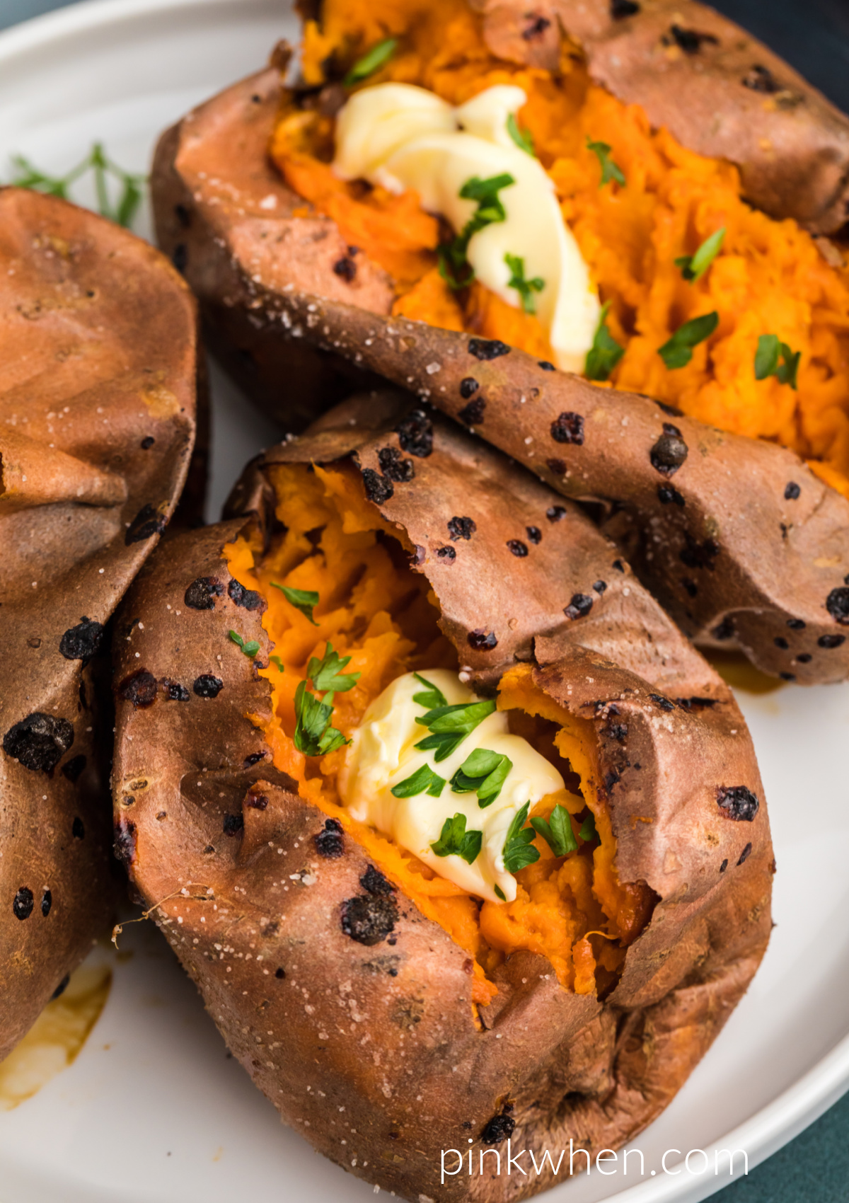 Air Fryer Baked Sweet Potatoes on a white plate ready to eat - topped with butter and fresh parsley. 