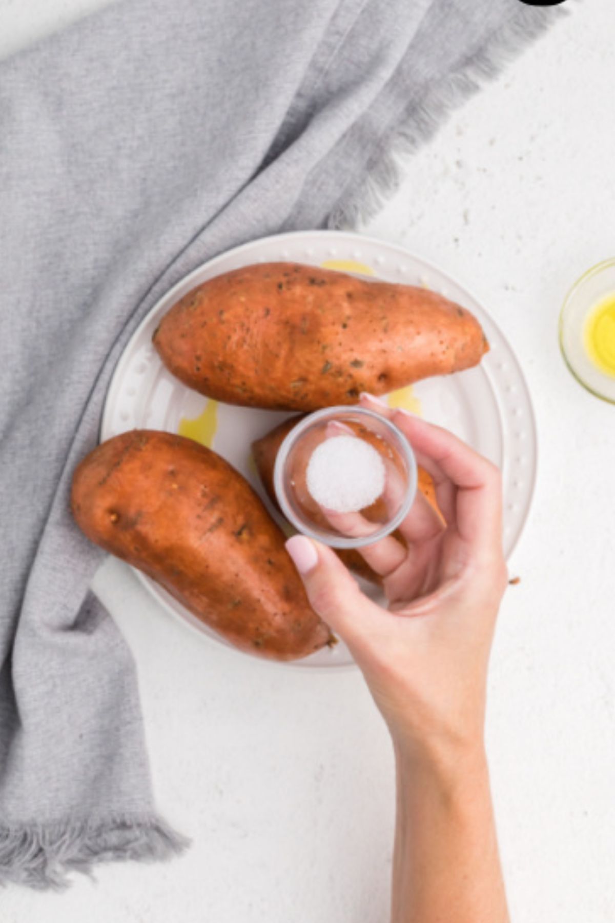 Olive oil and salt being rubbed on uncooked sweet potatoes