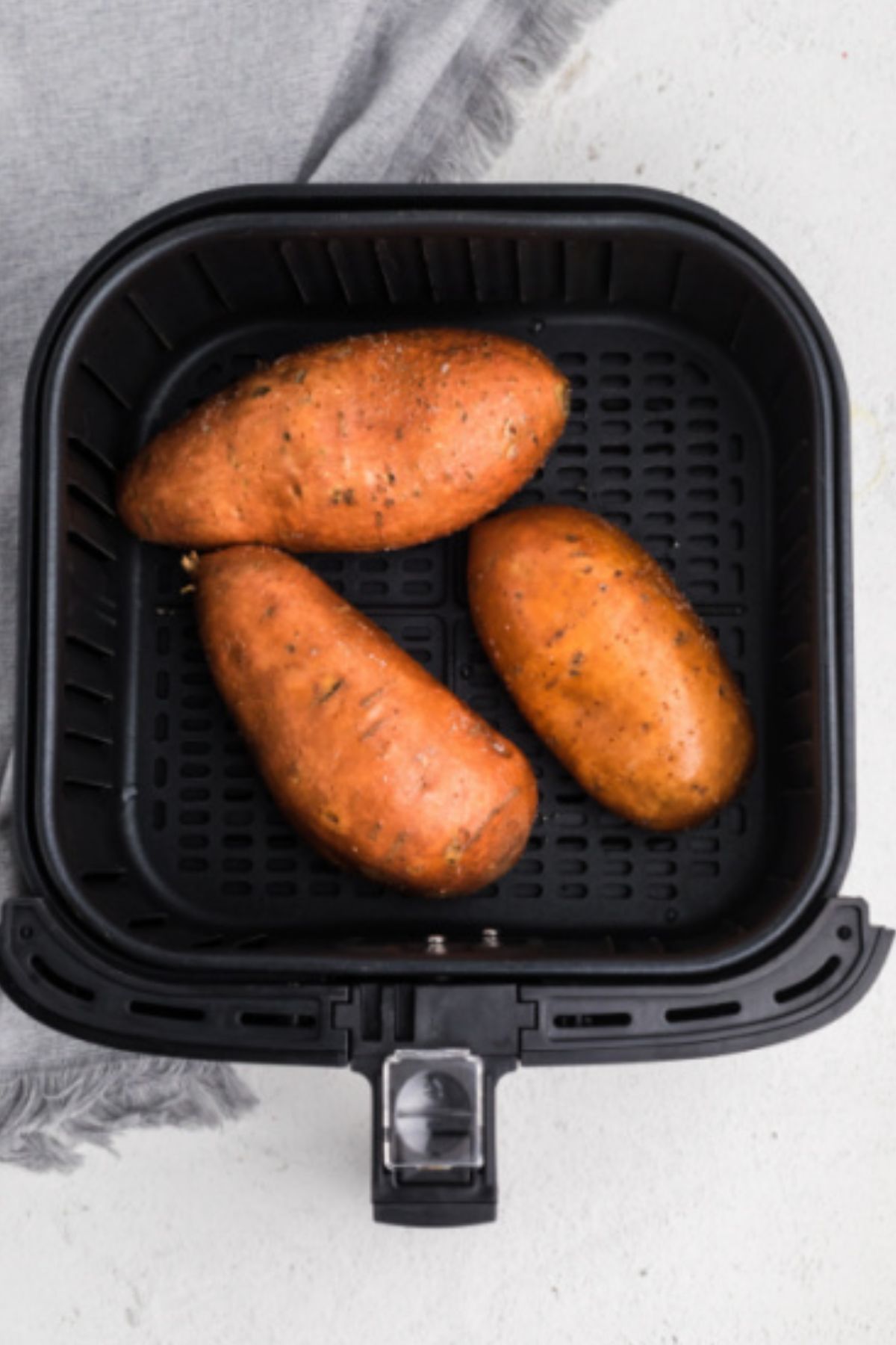 Uncooked seasoned sweet baked potatoes in the air fryer basket. 