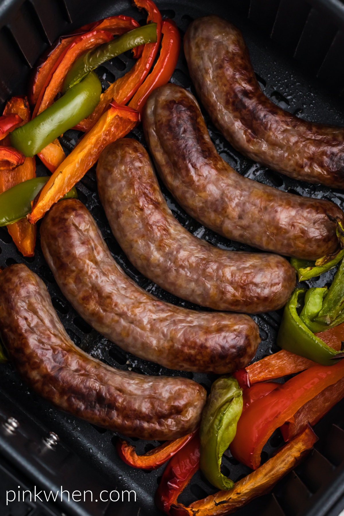Cooked brats and bell peppers in the basket of the air fryer. 