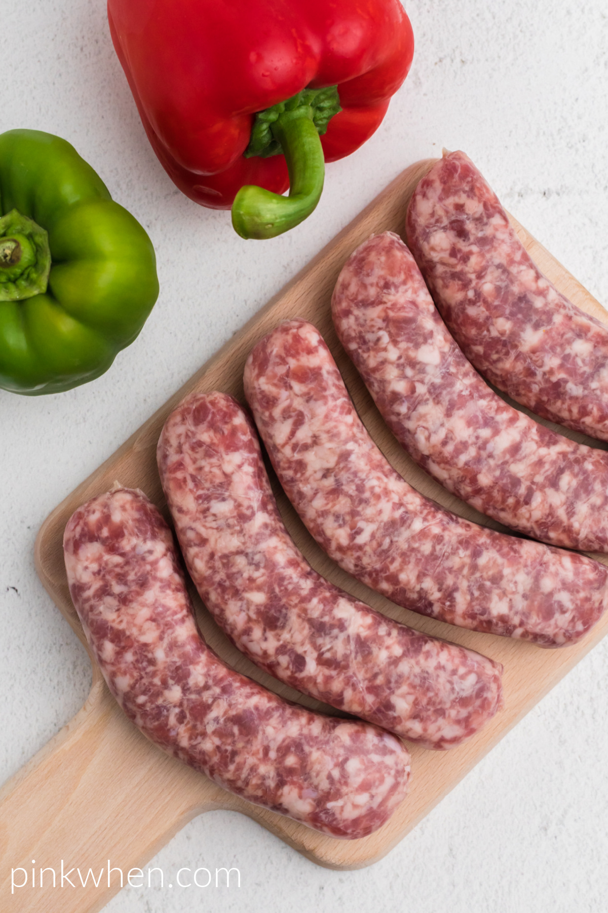 Brats and bell peppers on a table, with brats on the cutting board. 