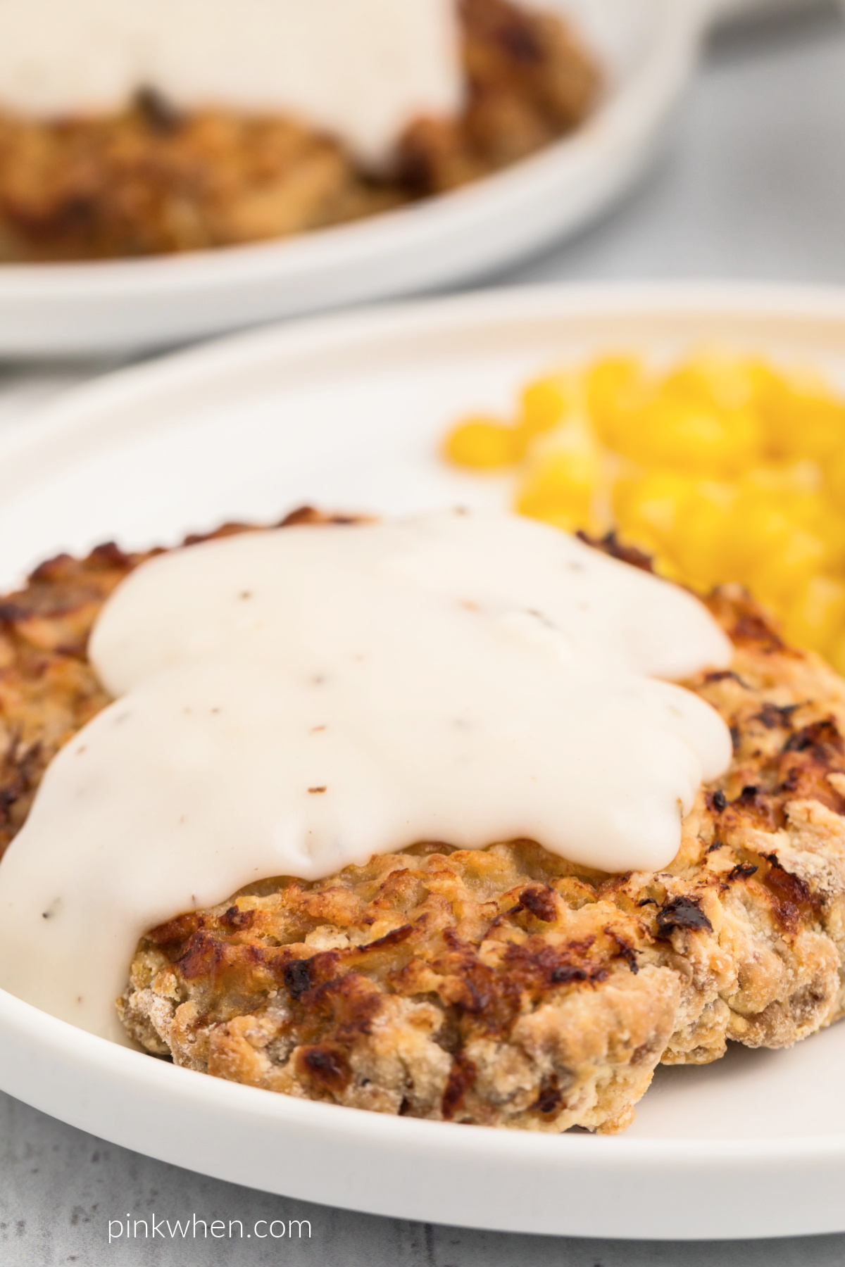 Air Fryer Chicken Fried Steak with white gravy and a side of corn on a white plate. 