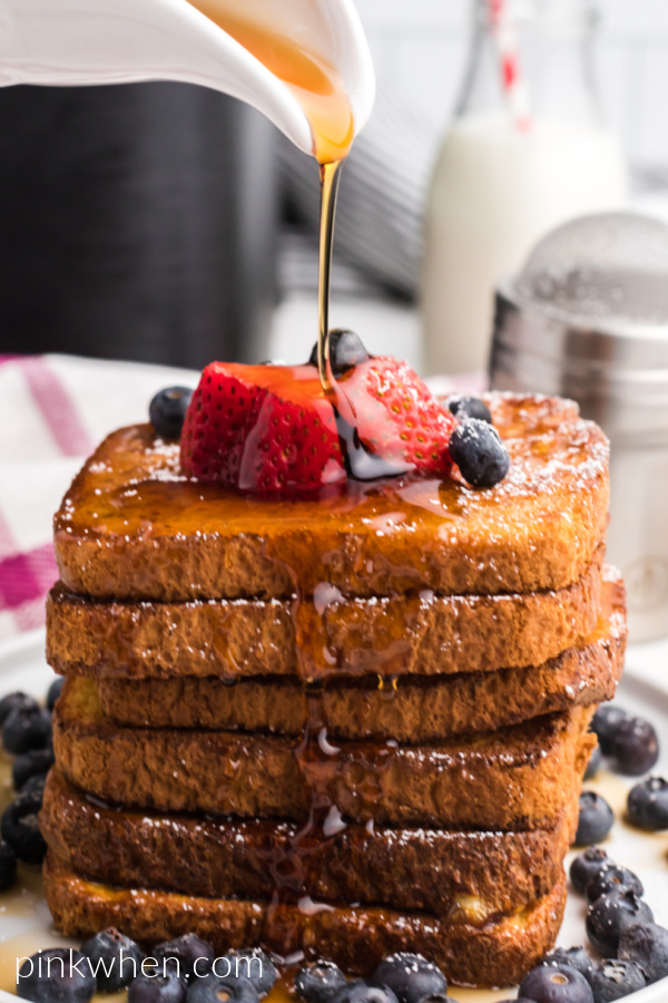 French Toast topped with fresh fruit, confectioners' sugar, and being topped with real maple syrup. 