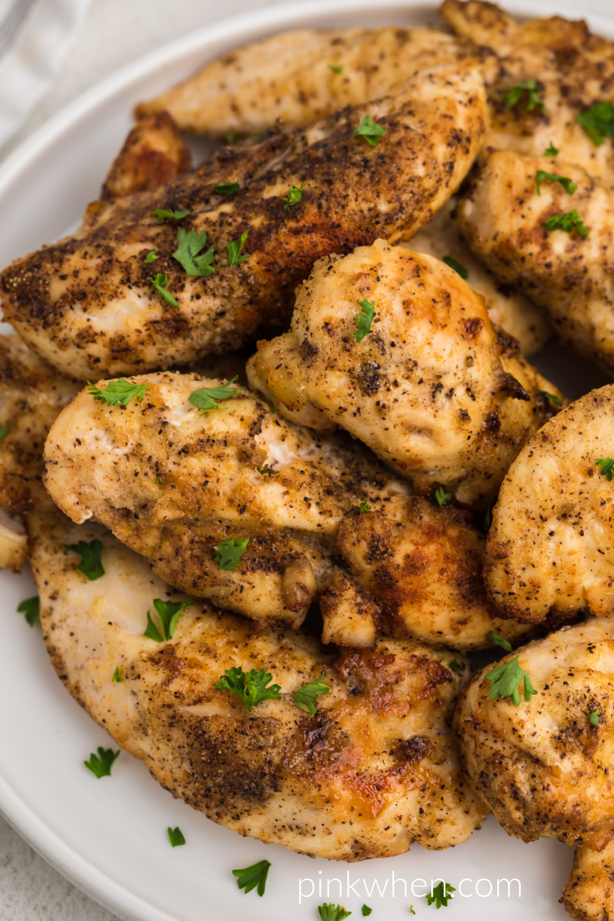 Seasoned air fryer grilled chicken tenders garnished with fresh parsley on a white plate.