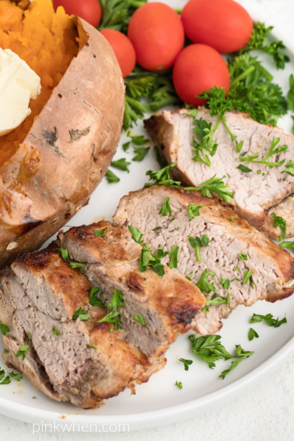 Pork tenderloin on a white plate served with a sweet potato and garnished with fresh chopped parsley. 