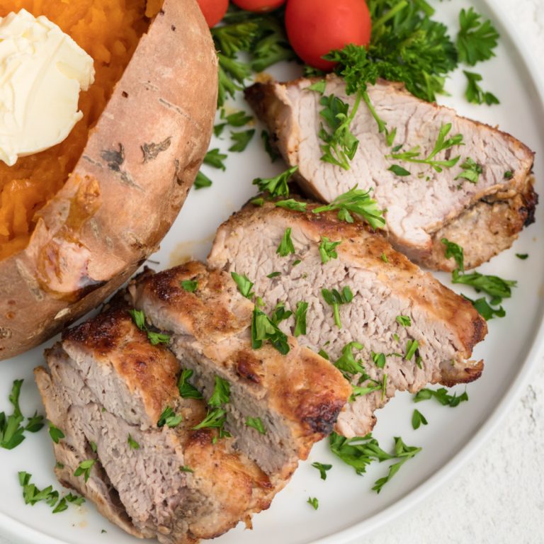 Air Fryer Pork Tenderloin on a white plate and garnished with fresh parsley.