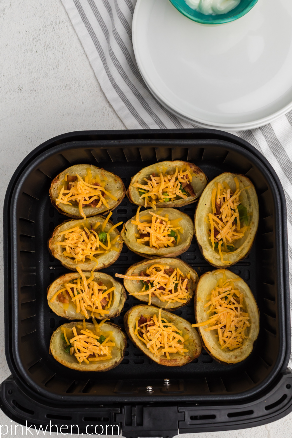 Potato skins loaded with cheese, bacon, and green onion tops ready to be cooked in the air fryer.
