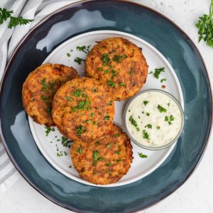 Overhead shot of air fryer salmon patties on a white plate with blue charger underneath, and a side of tartar sauce.