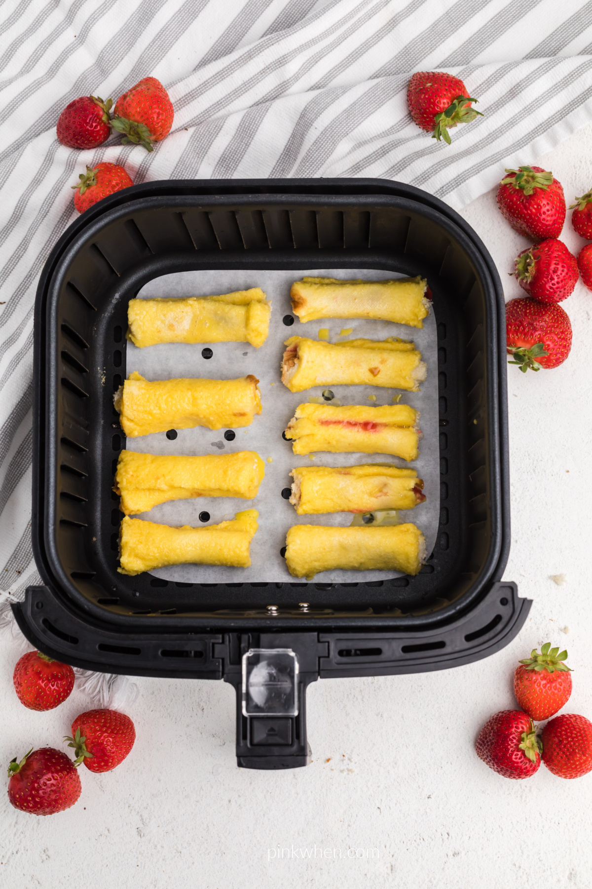 strawberry french toast roll ups in the basket of the air fryer on a piece of parchment paper. 