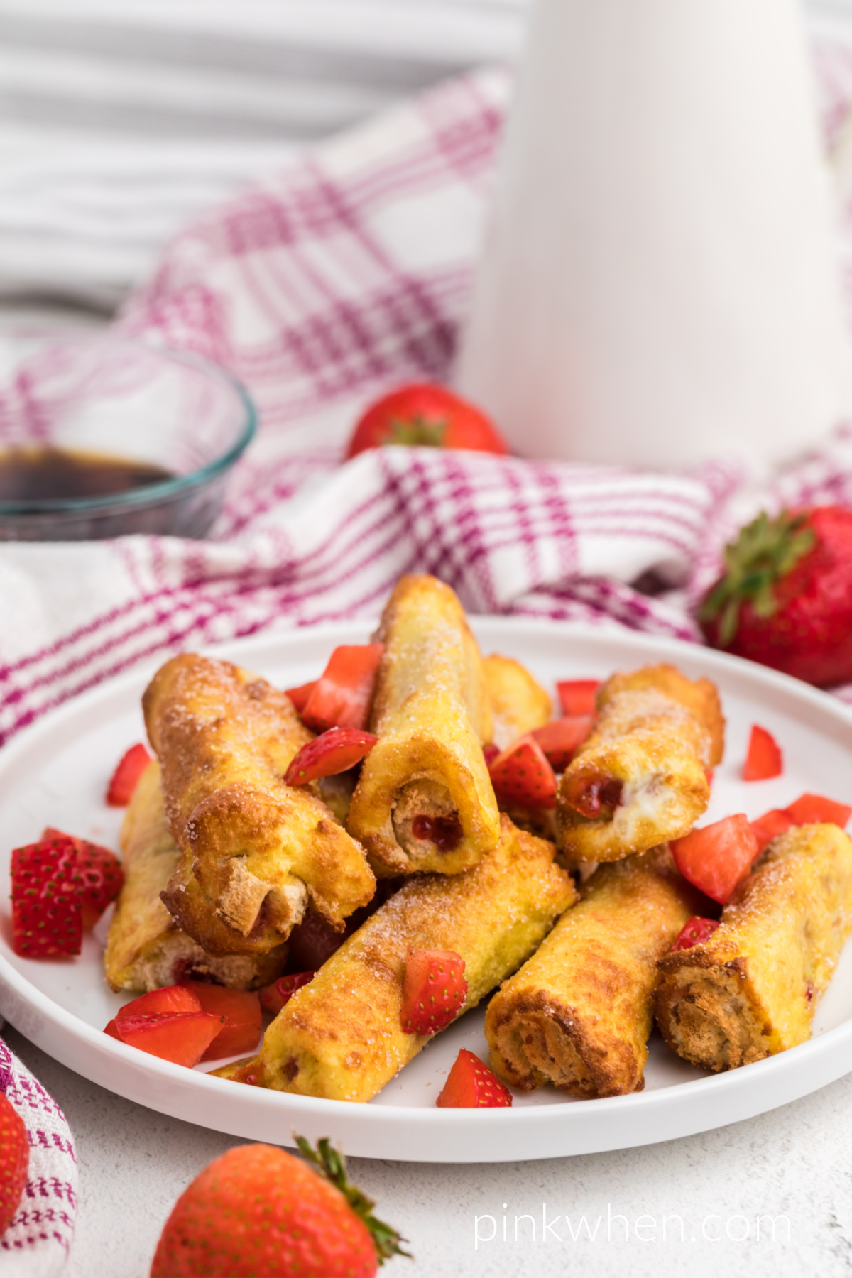 Strawberry French Toast Roll Ups made in the air fryer and served on a white plate with fresh chopped strawberries.