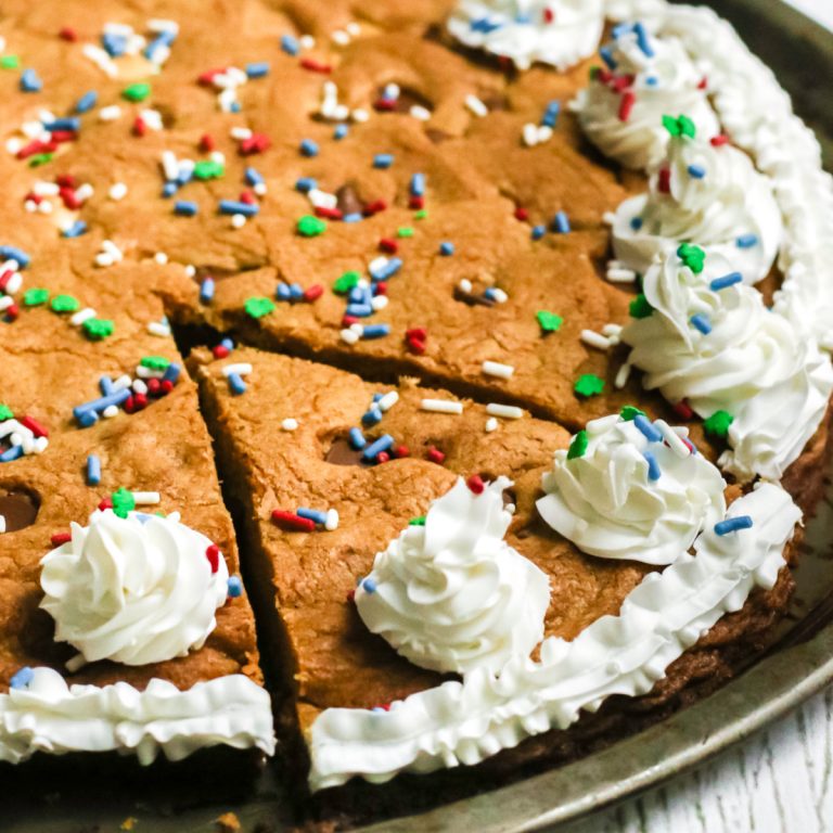 chocolate chip cookie cake on a pan with a slice cut and ready to serve.