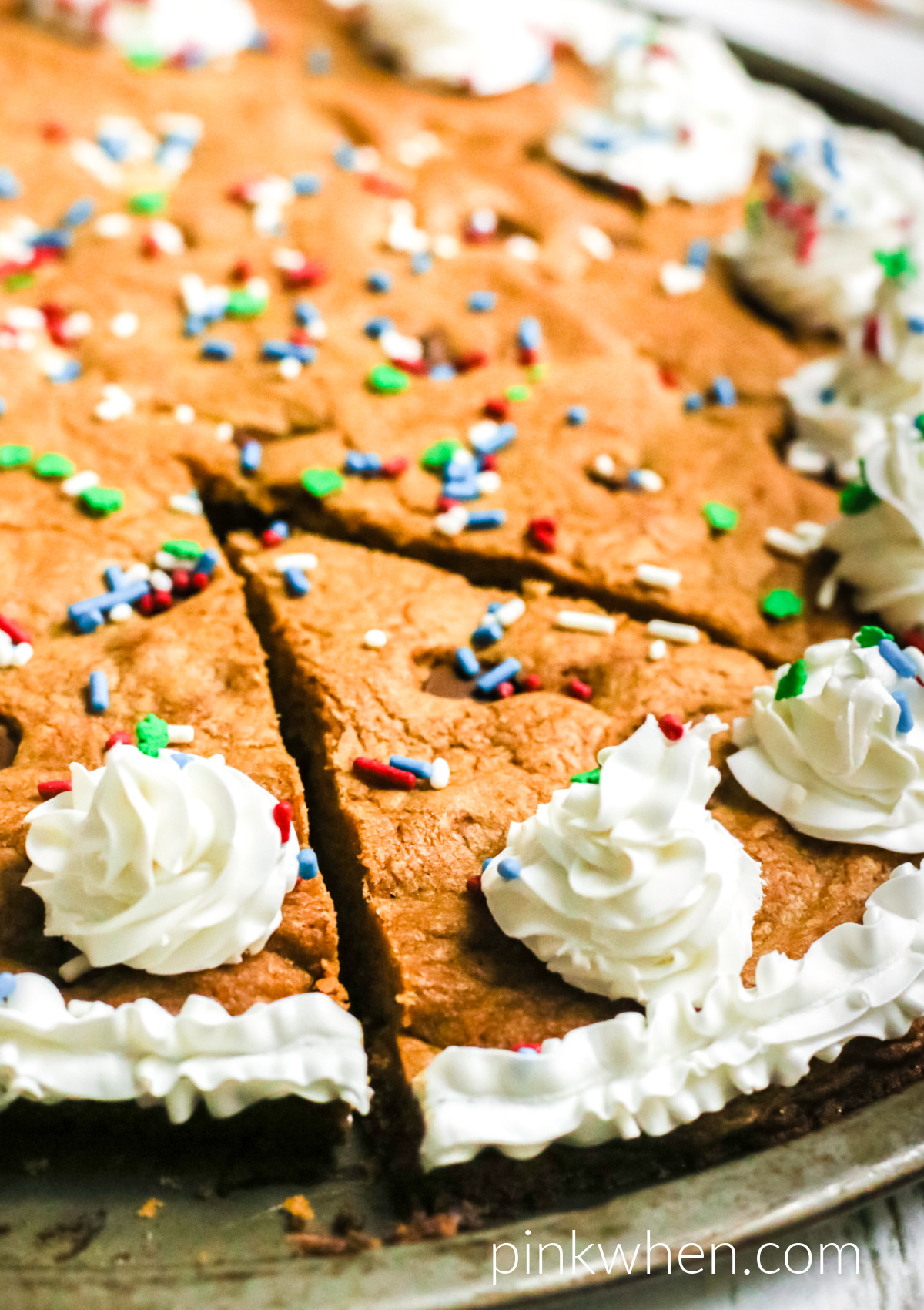 Homemade chocolate chip cookie cake on a pan and topped with frosting and sprinkles and ready to serve. 