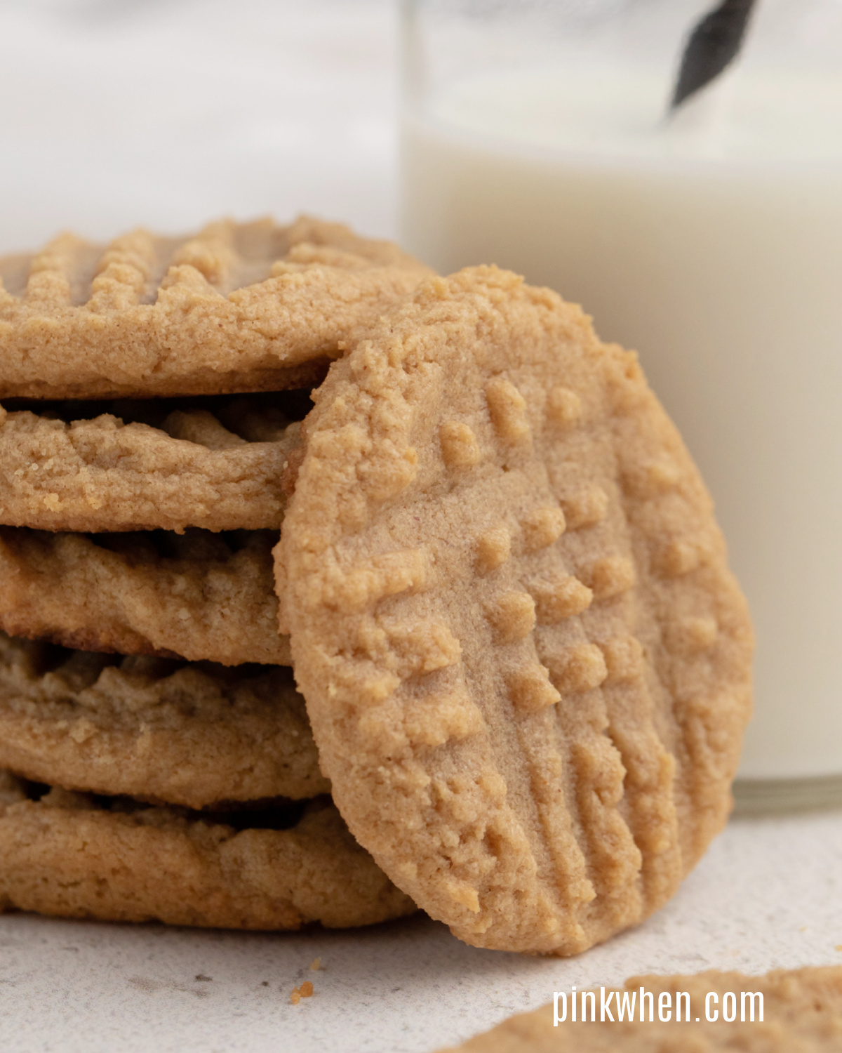 Close up photo of peanut butter cookies stacked next to a glass of milk. 