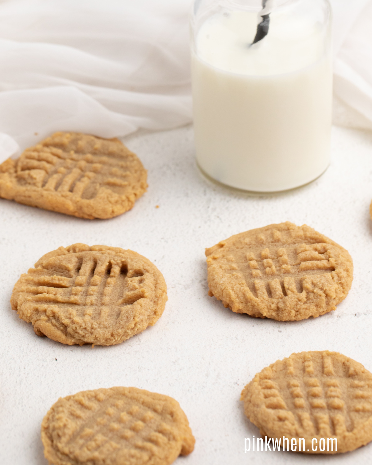 Peanut butter cookies laid out on a table with a glass of milk. 