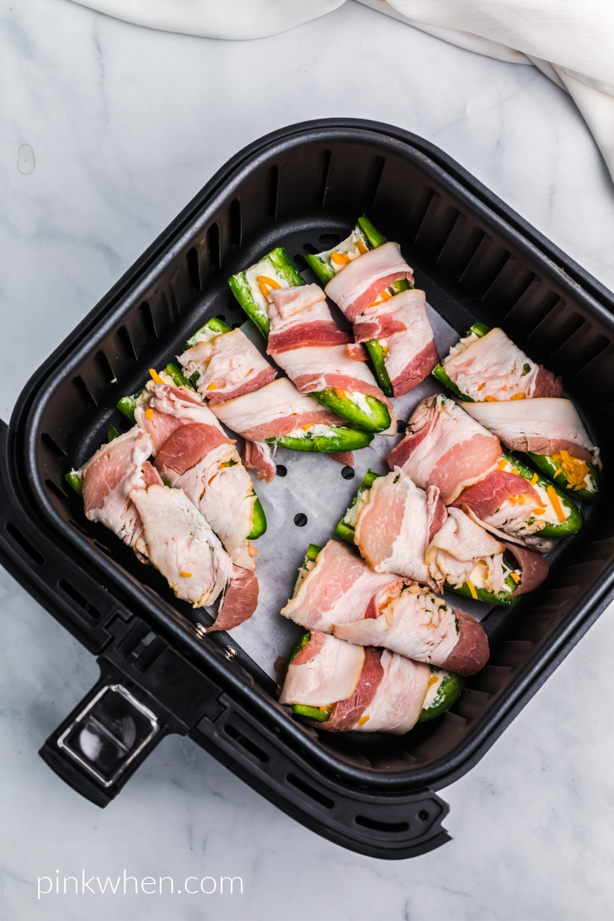Bacon wrapped jalapenos in the basket of the air fryer ready to cook. 