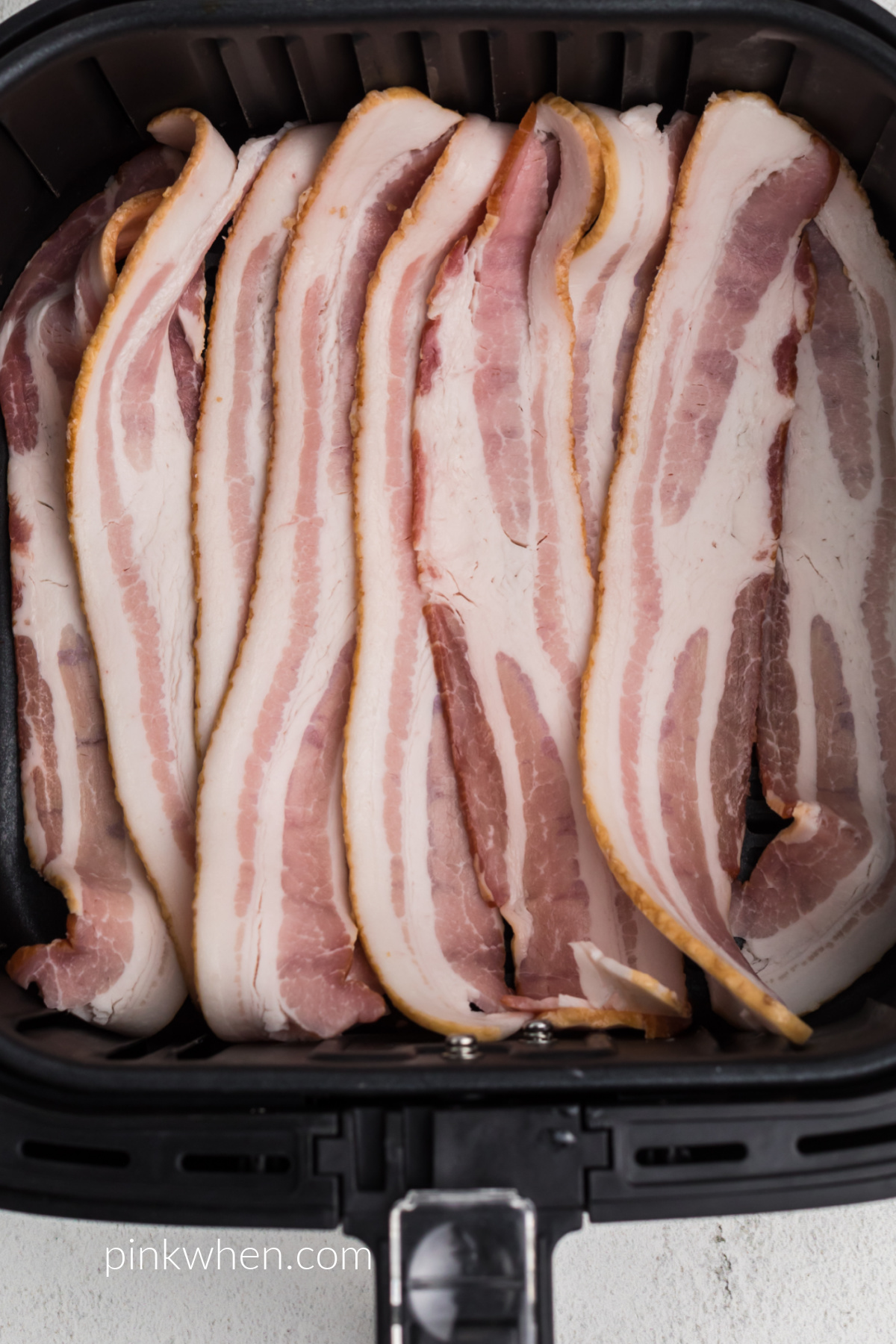 Uncooked bacon in the basket of the air fryer. 