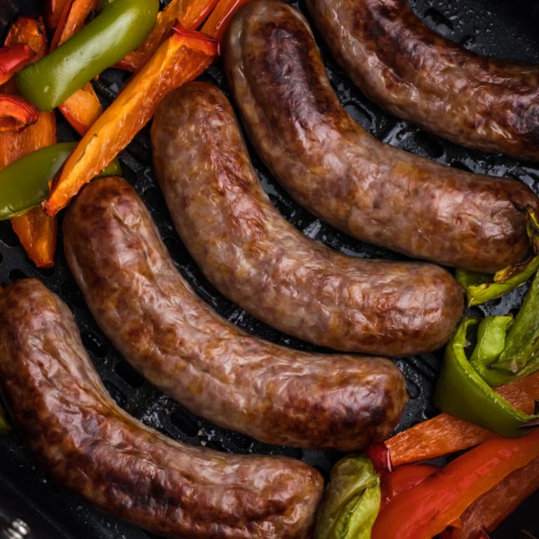 brats and bell peppers fully cooked in the basket of the air fryer.