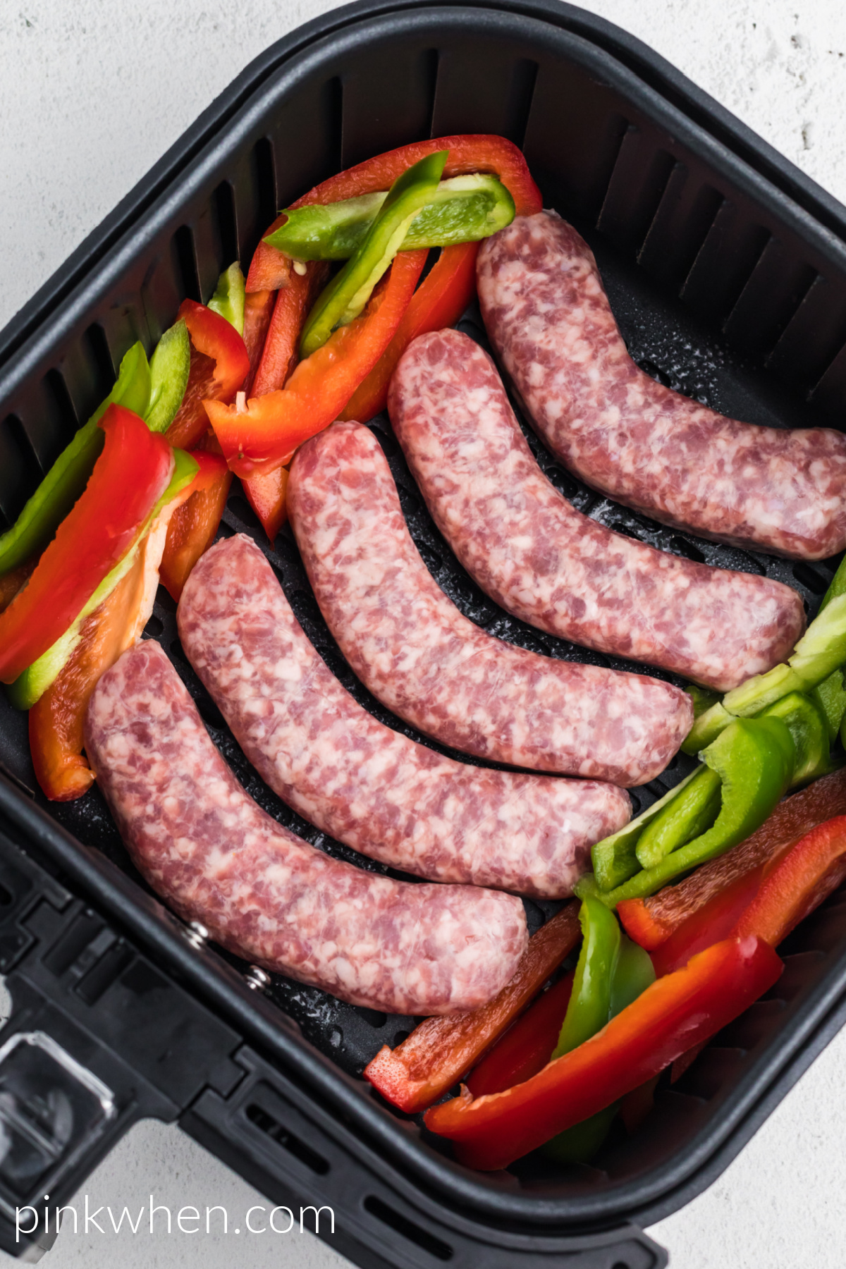 bell peppers and brats in the air fryer basket, ready to cook. 