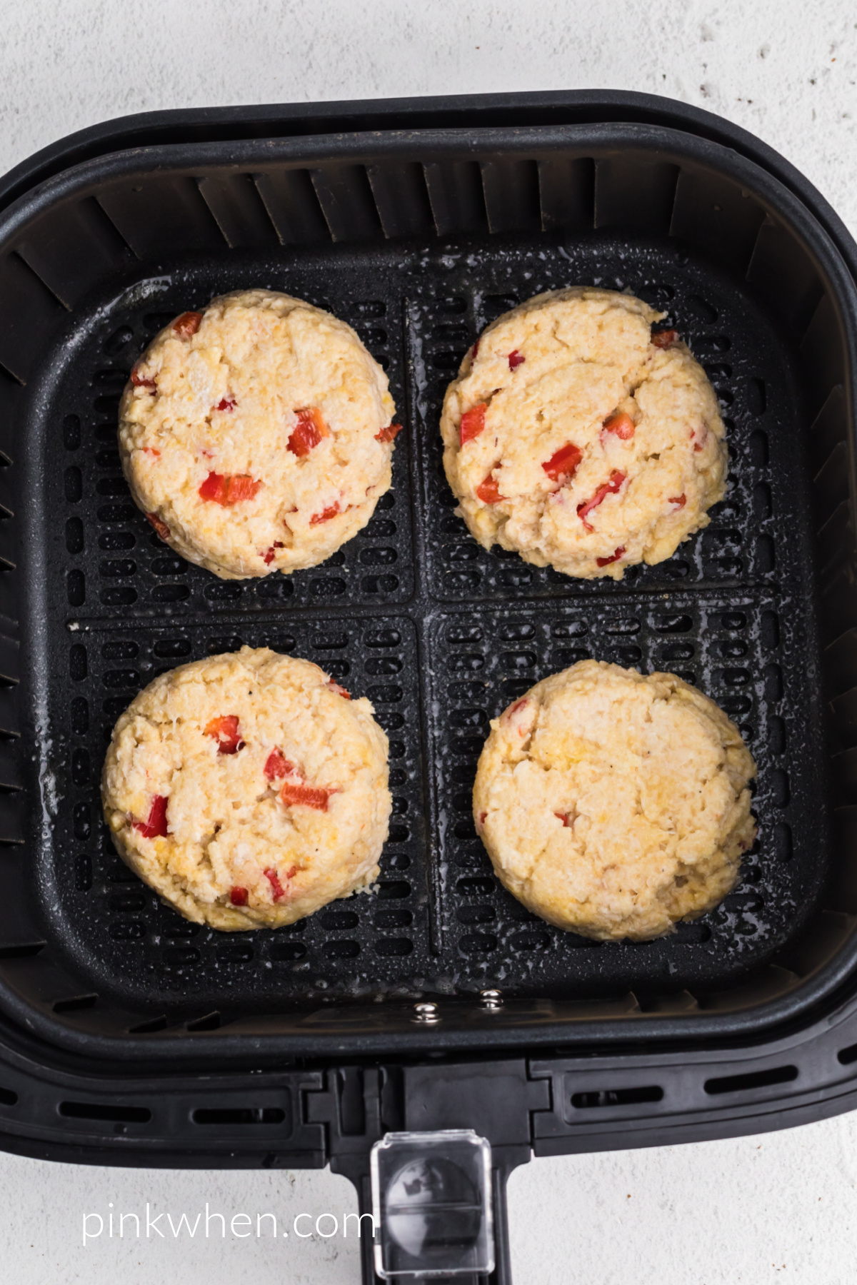 crab cake patties in the air fryer basket ready to cook.